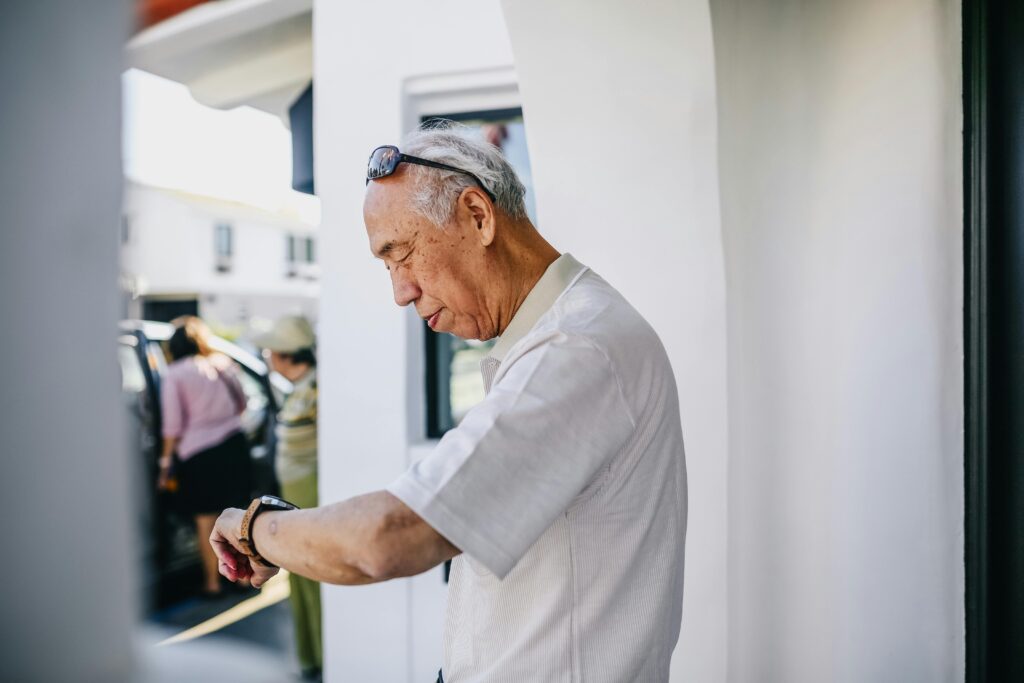 Senior Asian man in white shirt looking at wristwatch. Outdoor setting with focus on time awareness.